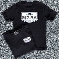 Two Blue Collar Kid black youth short sleeve tees on a gravel surface (shows front and back). Small imprint on the left front "pocket" area. Design says "Blue Collar Kid. Just. Like. Dad."