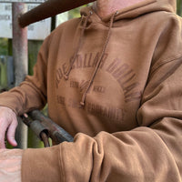 Man, outdoors, pictured close up wearing a WW "Blue Collar Dollar. Blood. Sweat. Profanity." graphic design on a brown hoodie, screenprinted in brown ink. "Stealth" effect.