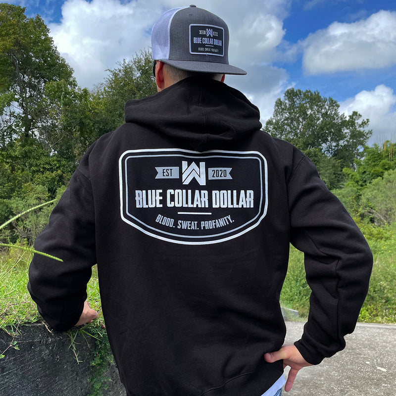 Man pictured from back, outdoors, wearing a WW Blue Collar Dollar black hooded pullover sweatshirt. "BLUE COLLAR DOLLAR. BLOOD. SWEAT. PROFANITY." design is printed on the back in white ink. Banded cuffs and waist. 