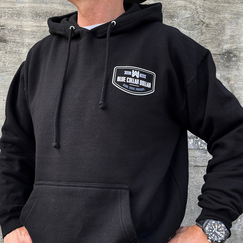 Man pictured from front wearing a WW Blue Collar Dollar black hoodie. WW "BLUE COLLAR DOLLAR. BLOOD. SWEAT. PROFANITY." design is printed in white, smaller on chest left "pocket" area. Banded cuffs and waist.