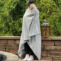 Woman standing outdoors with an oversized We Workin Athletic Grey Fleece Stadium blanket with Script logo-style wrapped around her.