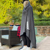 Woman standing outdoors with an oversized We Workin Dark Grey Fleece Stadium blanket with Block logo-style wrapped around her.