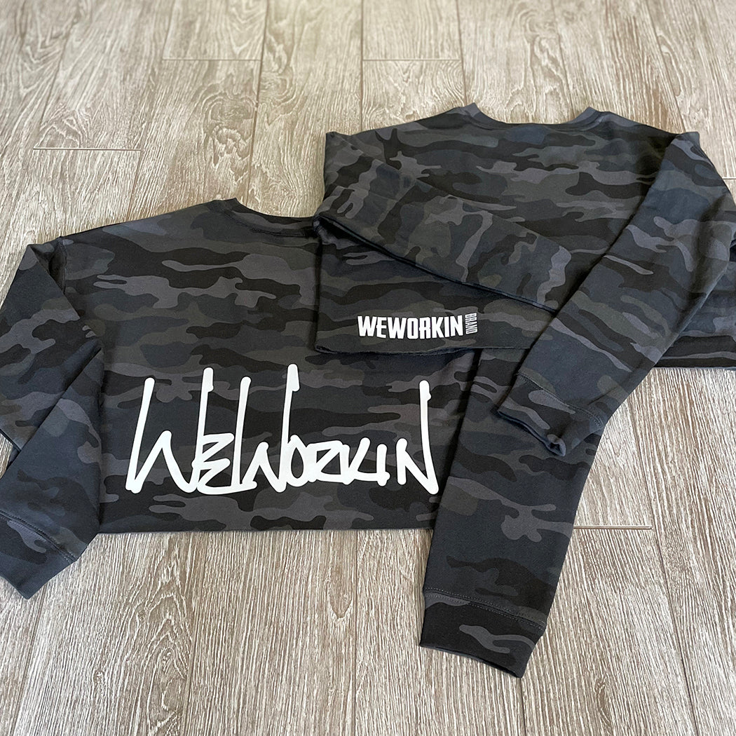 We Workin women's lightweight cropped crew pullover in Black Camo, available in 2 graphic options—BACK PRINTS ONLY—1 option is the "WEWORKIN" Script in white ink, and 1 option is the WWB horizontal block logo in white/grey ink. [Designs approx 5.5" to 13" wide.]