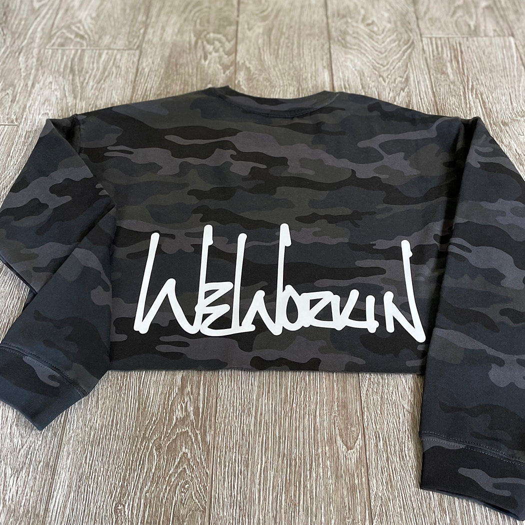 Back view of the We Workin women's lightweight cropped crew pullover in Black Camo (back print only, no front print). WEWORKIN Script logo is printed large across the back, bottom hem area in white ink. Imprint approx 13" wide.