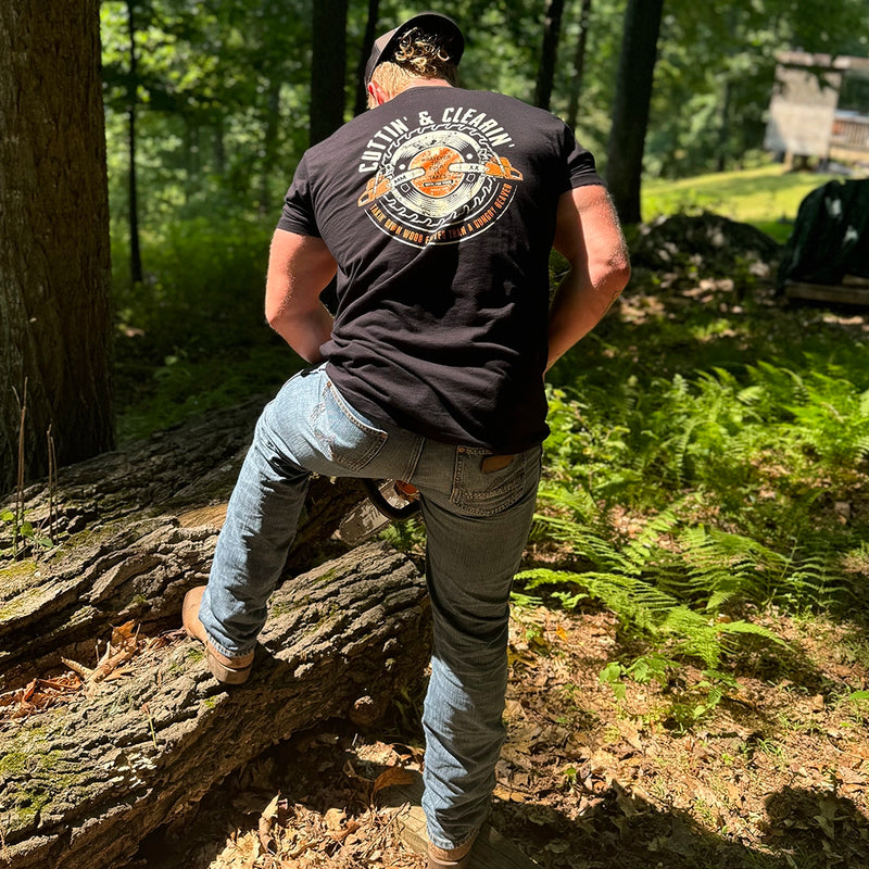 Man wearing a WW black tee, shown from back, cutting wood with a chainsaw. "CUTTIN' & CLEARIN'—Takin' Down Wood Faster than A Hungry Beaver" text encircles a graphic of chainsaws and circular blade (additional text in the center of saw blade: Whatever the F*ck It Takes, Made For Wood). Printed in Off-white and Burnt Orange inks. Graphic is printed large on the centerback.