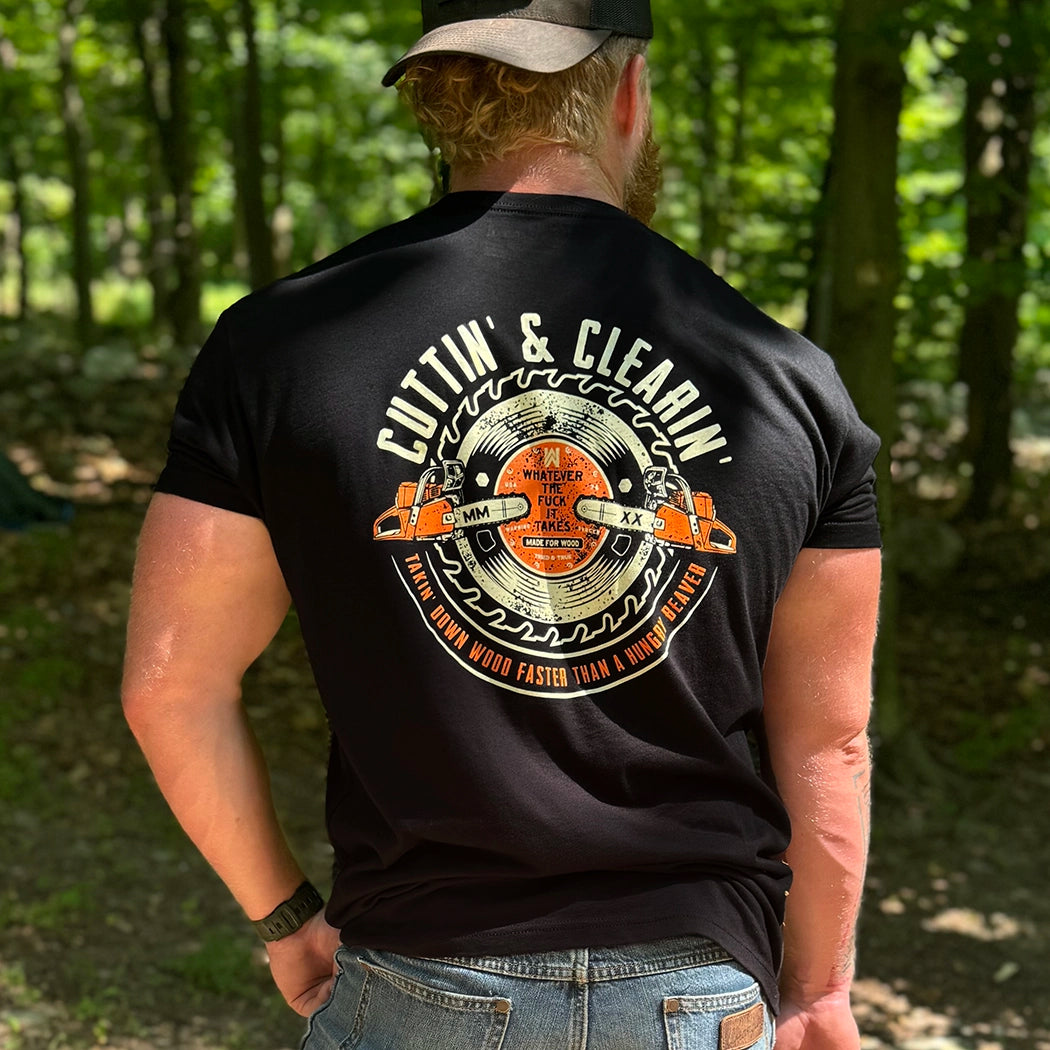 Man wearing a WW black tee, shown from back, in the woods. "CUTTIN' & CLEARIN'—Takin' Down Wood Faster than A Hungry Beaver" text encircles a graphic of chainsaws and circular blade (additional text in the center of saw blade: Whatever the F*ck It Takes, Made For Wood). Printed in Off-white and Burnt Orange inks. Graphic is printed large on the centerback.