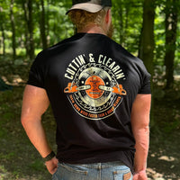 Man wearing a WW black tee, shown from back, in the woods. "CUTTIN' & CLEARIN'—Takin' Down Wood Faster than A Hungry Beaver" text encircles a graphic of chainsaws and circular blade (additional text in the center of saw blade: Whatever the F*ck It Takes, Made For Wood). Printed in Off-white and Burnt Orange inks. Graphic is printed large on the centerback.