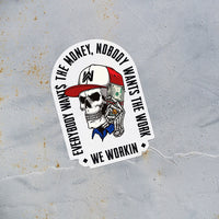 EVERYBODY WANT$ THE MONEY, NOBODY WANTS THE WORK. WE WORKIN—Die-cut sticker. "EWTM" tagline and WE WORKIN text, surrounding a Skull wearing a hat and holding a money bundle to his ear. Skull graphic in color, text in black. EWTM Arch design on white sticker, put on a rusted metal wall.