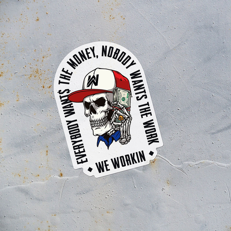 EVERYBODY WANT$ THE MONEY, NOBODY WANTS THE WORK. WE WORKIN—Die-cut sticker. "EWTM" tagline and WE WORKIN text, surrounding a Skull wearing a hat and holding a money bundle to his ear. Skull graphic in color, text in black. EWTM Arch design on white sticker, put on a rusted metal wall.