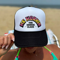 Woman wearing a WeWorkin Foam Trucker Snapback Hat in Black/White/Black colorway, pictured outdoors from front. Design shows WE WORKIN text in Neon Vibe colors arched over THE WORKIN CLASS stacked text. MM and XX are on the left and right respectively.