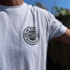 Man from front, wearing a WW white tee. 1-color black, distressed circular design, "GET HARD" main text in center of layout, "WE WORKIN" and "Never Easy Always Worth It" on the top and bottom of circular design, and finally "Hard Workin" and "Hard Livin" in center top/bottom—printed small in the left chest "pocket" area.