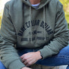 Man pictured from front wearing a WW "Blue Collar Dollar. Blood. Sweat. Profanity." arched graphic on a Military Green hoodie, screen printed in black ink on front only. 