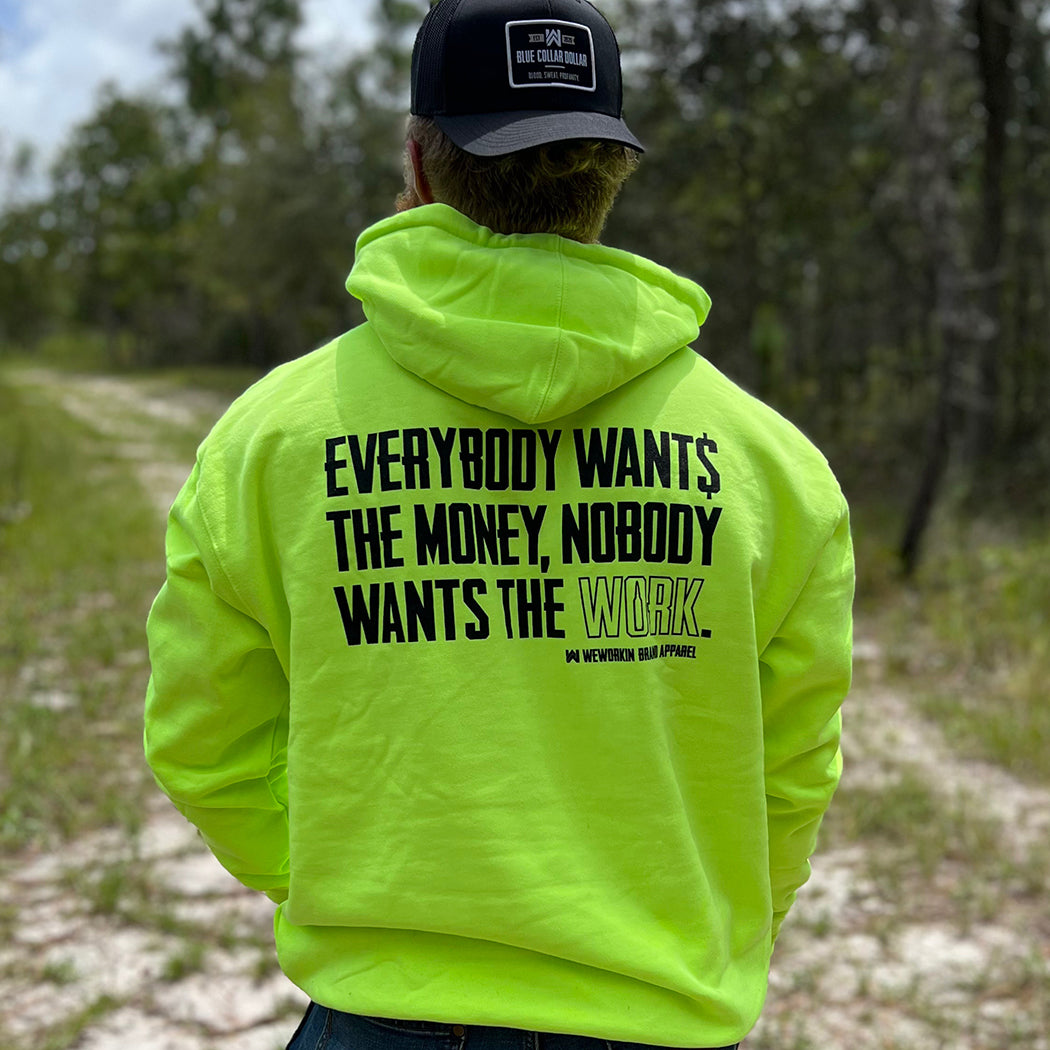 Man pictured from back wearing a We Workin premium Safety Yellow hoodie. "EVERYBODY WANT$ THE MONEY, NOBODY WANTS THE WORK" printed large on the back in black ink, and the word WORK is outlined in white for emphasis. (WEWORKIN BRAND APPAREL printed small and lower right just below the full back imprint.)