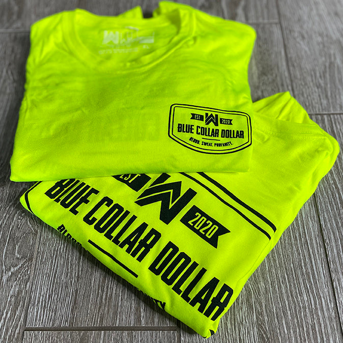 2 folded/stacked We Workin Hi-Viz long sleeve tees in Safety Yellow on wood tile background. Front of tee is printed with the We Workin BLUE COLLAR DOLLAR. BLOOD. SWEAT. PROFANITY. design in smaller left "pocket" size and back is same design but large, both printed in Black ink.