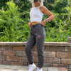 Woman pictured from front-left side wearing the We Workin women's joggers in Heathered Charcoal Grey. "NOT FOR THE WEAK" white text encircling the WW icon logo in bright pink, subtly printed just below the front left pocket area. [Design approx 2.25" wide.]