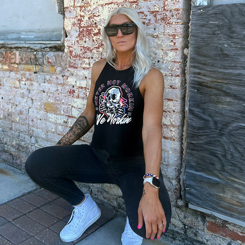 Woman wearing a WW black cropped racerback tank, shown from front. "NEVER NOT WORKIN" text arching around the top and sides of a Neon Skull "bustin out" as center image. WE WORKIN is along the bottom of the graphic in script. Graphic is printed large on the center front (no back print). Printed in white and multiple Neon inks.