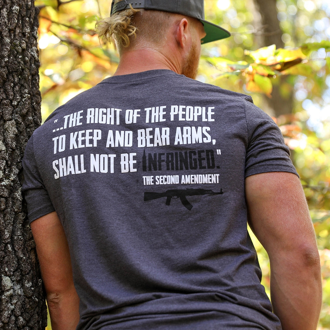 Man pictured from back wearing a We Workin graphic tee in Steel Grey color. Back imprinted with a partial quote from the Second Amendment—...the right of the people to keep and bear Arms, shall not be infringed—printed in white ink with the word INFRINGED highlighted in BLACK. "The Second Amendment" is printed smaller, in white, in the lower right corner with an AR printed underneath that in black ink.