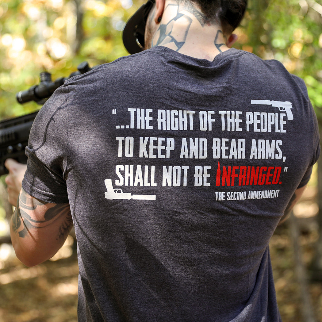 Man pictured from back wearing a We Workin graphic tee in Steel Grey color. Back imprinted with a partial quote from the Second Amendment—...the right of the people to keep and bear Arms, shall not be infringed—printed in white ink with the word INFRINGED highlighted in Red. "The Second Amendment" is printed smaller, in white, in the lower right corner and handguns are on the top right and bottom left corners.