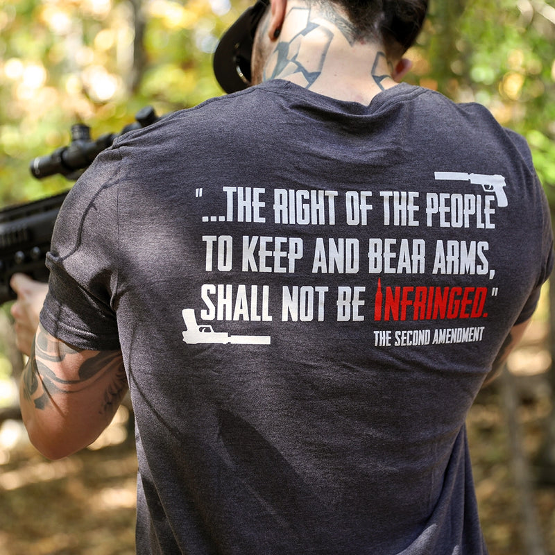 Man pictured from back wearing a We Workin graphic tee in Steel Grey color. Back imprinted with a partial quote from the Second Amendment—...the right of the people to keep and bear Arms, shall not be infringed—printed in white ink with the word INFRINGED highlighted in Red. "The Second Amendment" is printed smaller, in white, in the lower right corner and handguns are on the top right and bottom left corners.