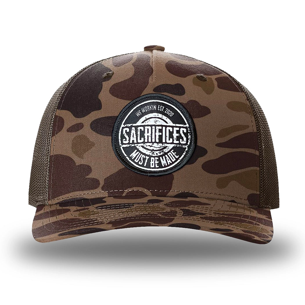 Bark Duck Camo/Brown two-tone WeWorkin hat—Richardson 112PFP snapback, 5-panel trucker, mesh-back style. WeWorkin "SACRIFICES MUST BE MADE" circular woven patch is centered on the front panel.