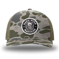 Marsh Duck Camo/Loden two-tone WeWorkin hat—Richardson 112PFP snapback, 5-panel trucker, mesh-back style. HARD WORK MATTERS woven patch with white merrowed edge, on a black background with HARD WORK MATTERS text encircling a Viking-style skull center graphic with MM XX on the left and right respectively—patch is centered on the front panels.