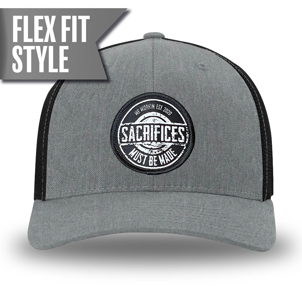 Heather Grey/Black Flex Fit style WeWorkin hat—Woven front with Poly mesh sides and back, Richardson 110 brand (R-Flex trucker). WeWorkin "SACRIFICES MUST BE MADE" circular woven patch is centered on the front panels.