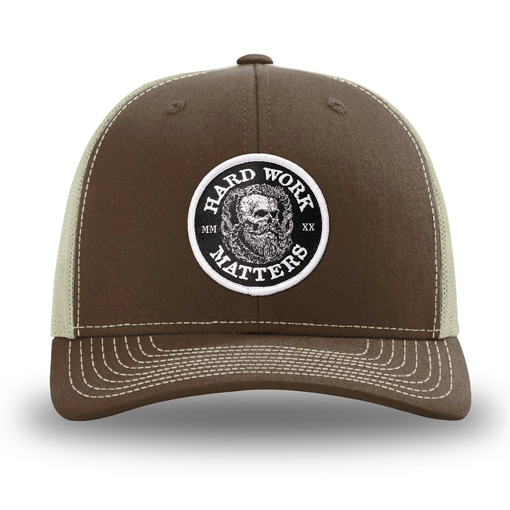 Brown/Khaki WeWorkin hat—Richardson 112 brand snapback, retro trucker classic hat style. HARD WORK MATTERS woven patch with white merrowed edge, on a black background with HARD WORK MATTERS text encircling a Viking-style skull center graphic with MM XX on the left and right respectively—patch is centered on the front panels.