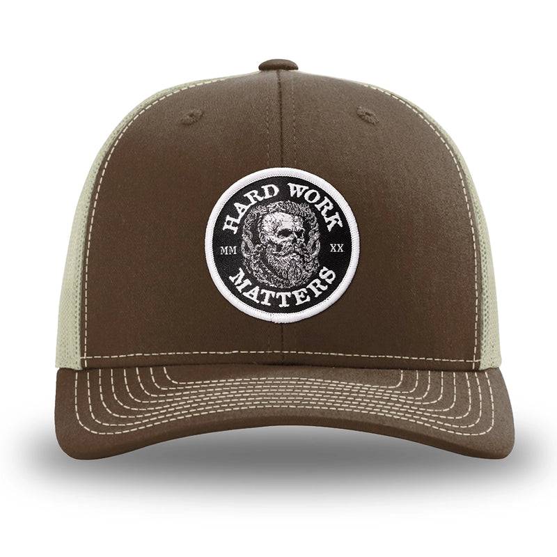 Brown/Khaki WeWorkin hat—Richardson 112 brand snapback, retro trucker classic hat style. HARD WORK MATTERS woven patch with white merrowed edge, on a black background with HARD WORK MATTERS text encircling a Viking-style skull center graphic with MM XX on the left and right respectively—patch is centered on the front panels.