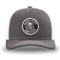 Charcoal/White WeWorkin hat—Richardson 112 brand snapback, retro trucker classic hat style. HARD WORK MATTERS woven patch with white merrowed edge, on a black background with HARD WORK MATTERS text encircling a Viking-style skull center graphic with MM XX on the left and right respectively—patch is centered on the front panels.