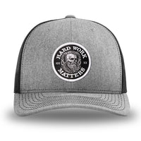 Heather Grey/Black WeWorkin hat—Richardson 112 brand snapback, retro trucker classic hat style. HARD WORK MATTERS woven patch with white merrowed edge, on a black background with HARD WORK MATTERS text encircling a Viking-style skull center graphic with MM XX on the left and right respectively—patch is centered on the front panels.