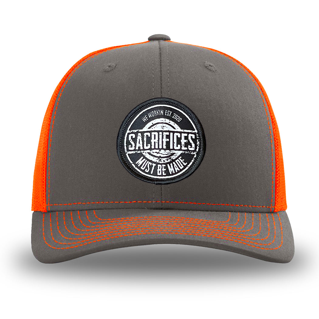 Neon/Safety Orange and Charcoal Grey two-tone WeWorkin hat—Richardson 112 brand snapback, retro trucker classic hat style. WeWorkin "SACRIFICES MUST BE MADE" circular woven patch is centered on the front panels.