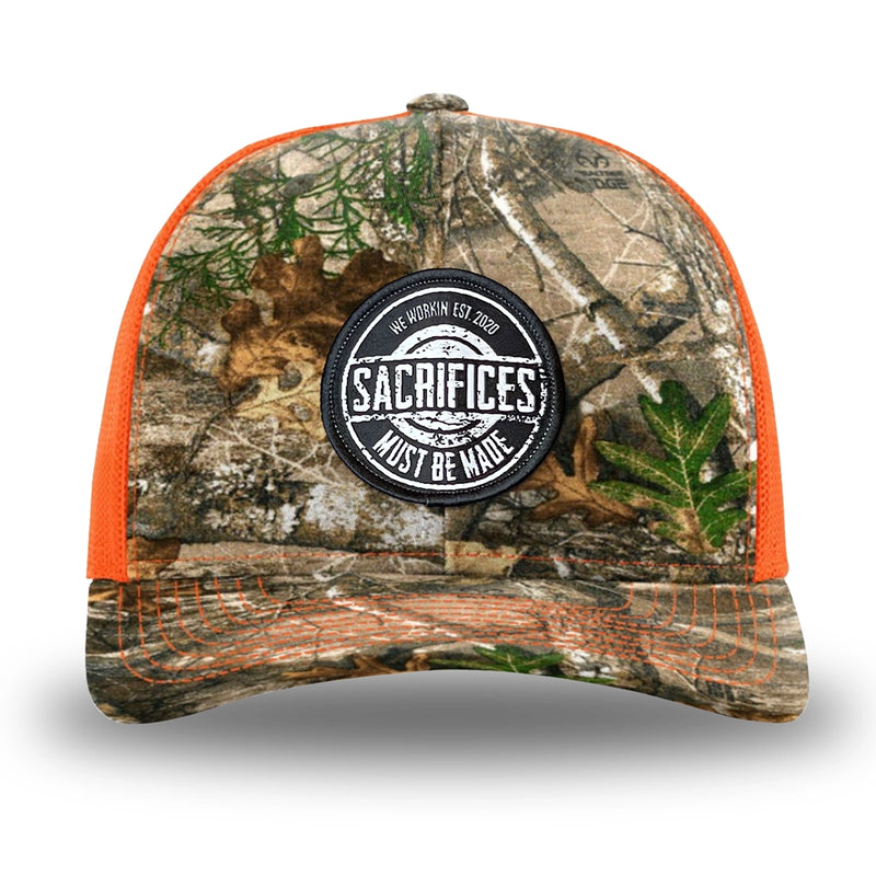 Neon Orange and RealTree Camo two-tone WeWorkin hat—Richardson 112 brand snapback, retro trucker classic hat style. WeWorkin "SACRIFICES MUST BE MADE" circular woven patch is centered on the front panels.