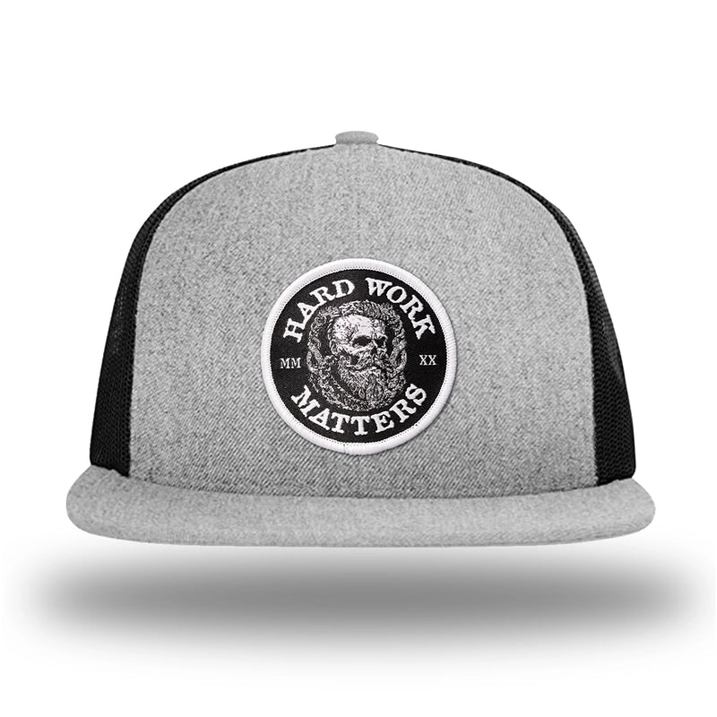 Heather Grey/Black WeWorkin hat—Richardson 511 brand snapback, flatbill trucker hat style. HARD WORK MATTERS woven patch with white merrowed edge, on a black background with HARD WORK MATTERS text encircling a Viking-style skull center graphic with MM XX on the left and right respectively—patch is centered on the front panels.