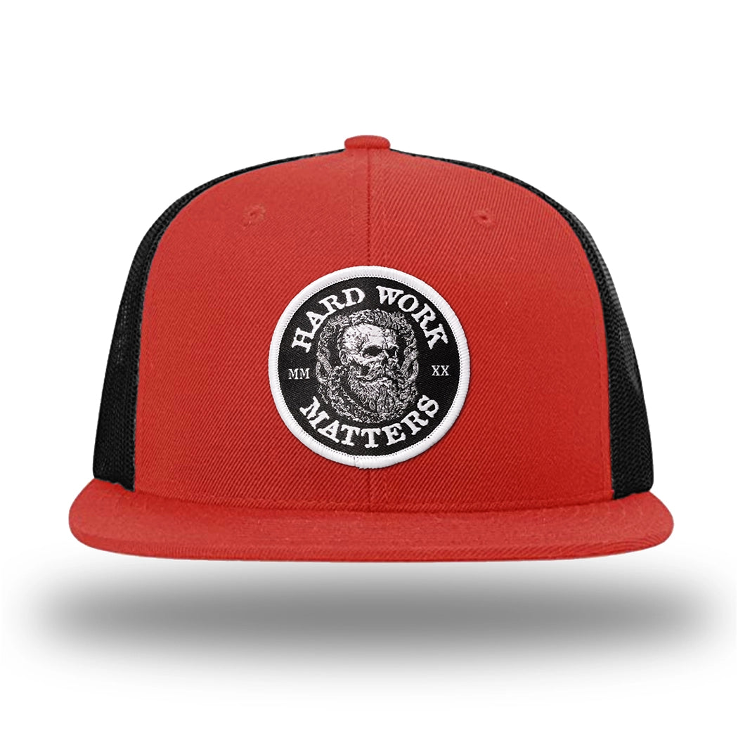 Red/Black WeWorkin hat—Richardson 511 brand snapback, flatbill trucker hat style. HARD WORK MATTERS woven patch with white merrowed edge, on a black background with HARD WORK MATTERS text encircling a Viking-style skull center graphic with MM XX on the left and right respectively—patch is centered on the front panels.