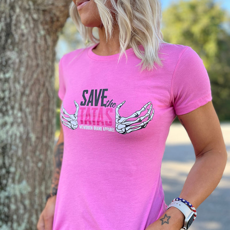 Woman pictured from front wearing a We Workin designed SAVE THE TATAS graphic on a bright pink fitted tee.