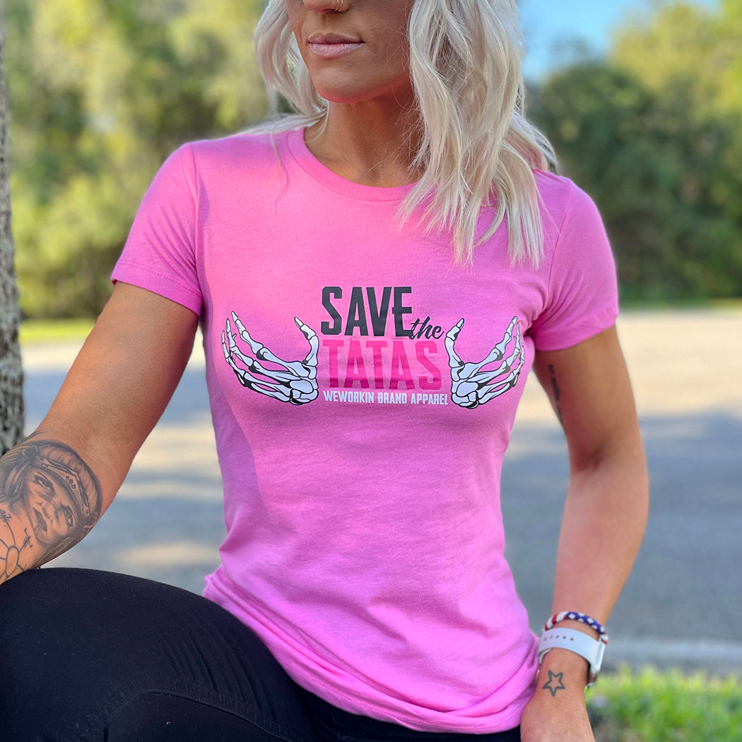 Woman pictured from front wearing a We Workin designed SAVE THE TATAS graphic on a bright pink fitted tee.