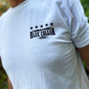 Man wearing a WW white tee pictured from front. "WE WORKIN. BLUE COLLAR COWBOY" text with stars on the top, printed small on the left chest "pocket" area, in black ink.