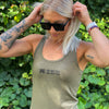 Woman pictured from front wearing a WEWORKIN racerback tank top in military green, with WEWORKIN WW icon on left and DO BETTER BE BETTER text stacked to the right imprinted small in black ink on the chest.