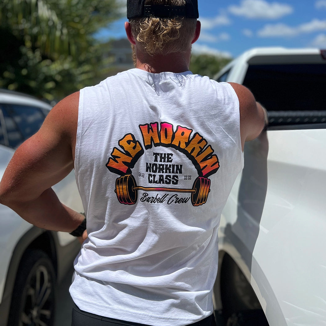 Man pictured from back, wearing a We Workin muscle tank in white. 3-color BARBELL CREW design in Neon Pink to Bright yellow fade and black, "WE WORKIN" main text is arched over top of "THE WORKIN CLASS" text and "Barbell Crew" script across the bottom—a Barbell in the center—design is printed large in the center back.