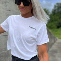 Front of a woman wearing a We Workin Women's short-sleeve cropped tee in white—with a small imprint of our "WEWORKIN BRAND" icon on the upper left chest in Black ink.