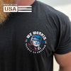 Man wearing a WW black tee MADE IN THE USA, shown from front. "WE WORKIN—SALUTE TO FREEDOM" text circling around a President Trump "freedom concepi" image in center. Graphic is printed small on left chest "pocket" area. Printed in full color/patriotic inks.