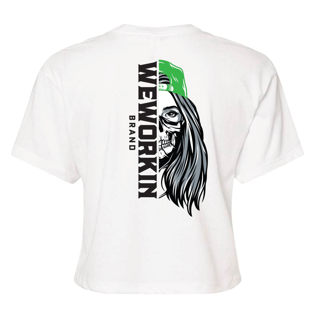 Back of a We Workin Women's short-sleeve cropped tee in white—with a large imprint of our "WEWORKIN BRAND vertical text and Half Skull Woman with Hat" design in Black/White/Grey (hat graphic highlighted in Lime Green ink.)