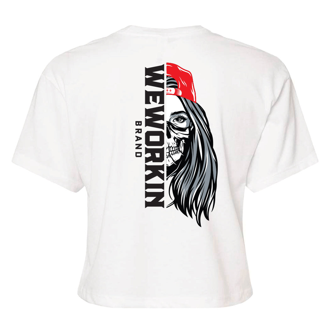 Back of a We Workin Women's short-sleeve cropped tee in white—with a large imprint of our "WEWORKIN BRAND vertical text and Half Skull Woman with Hat" design in Black/White/Grey (hat graphic highlighted in Bright Red ink.)