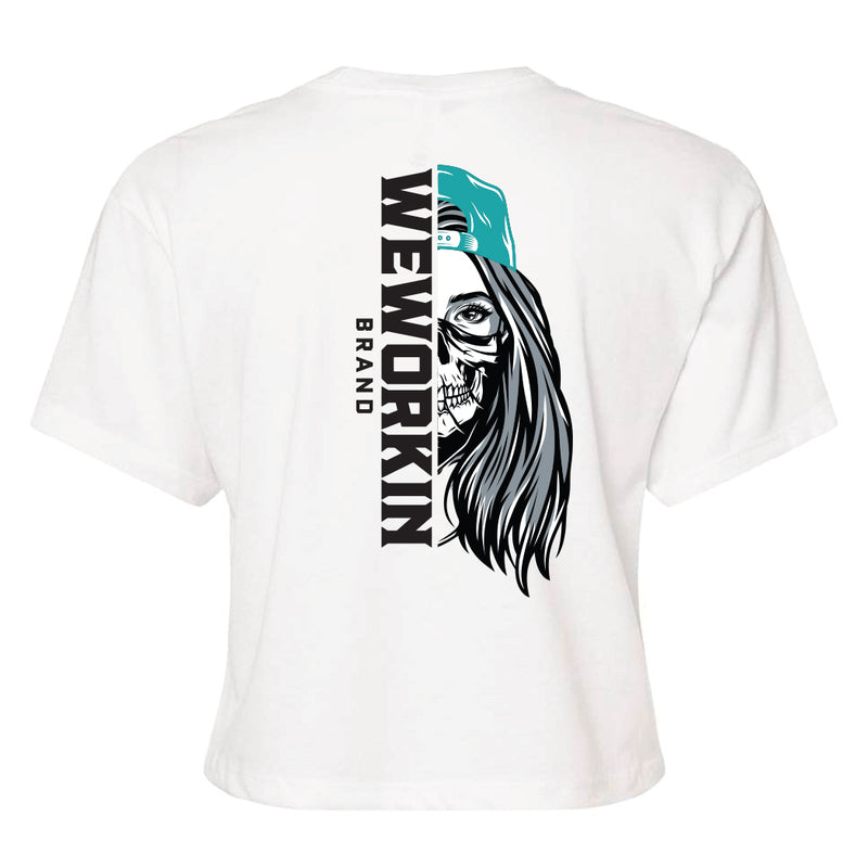 Back of a We Workin Women's short-sleeve cropped tee in white—with a large imprint of our "WEWORKIN BRAND vertical text and Half Skull Woman with Hat" design in Black/White/Grey (hat graphic highlighted in Teal ink.)