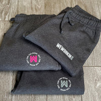 WWB Joggers available in 3 graphic options—front view of We Workin branded women's joggers (stacked) in Heathered Charcoal Grey, folded to show the printed logos. 2 options of the "NOT FOR THE WEAK" white text encircling the WW icon logos in grey or pink, and 1 option of the WWB horizontal block logo in white/grey ink—all subtly printed just below the front left pocket area. [Designs approx 2.25" to 3.5" wide.]