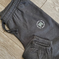 Front view of the We Workin women's joggers in Heathered Charcoal Grey, folded to show the printed logo. "NOT FOR THE WEAK" white text encircling the WW icon logo in grey, subtly printed just below the front left pocket area. [Design approx 2.25" wide.]