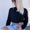 Woman, outside, pictured from front, wearing a We Workin women’s cropped long sleeved tee in black. Small printed WW icon on center chest near neckline, in white ink.