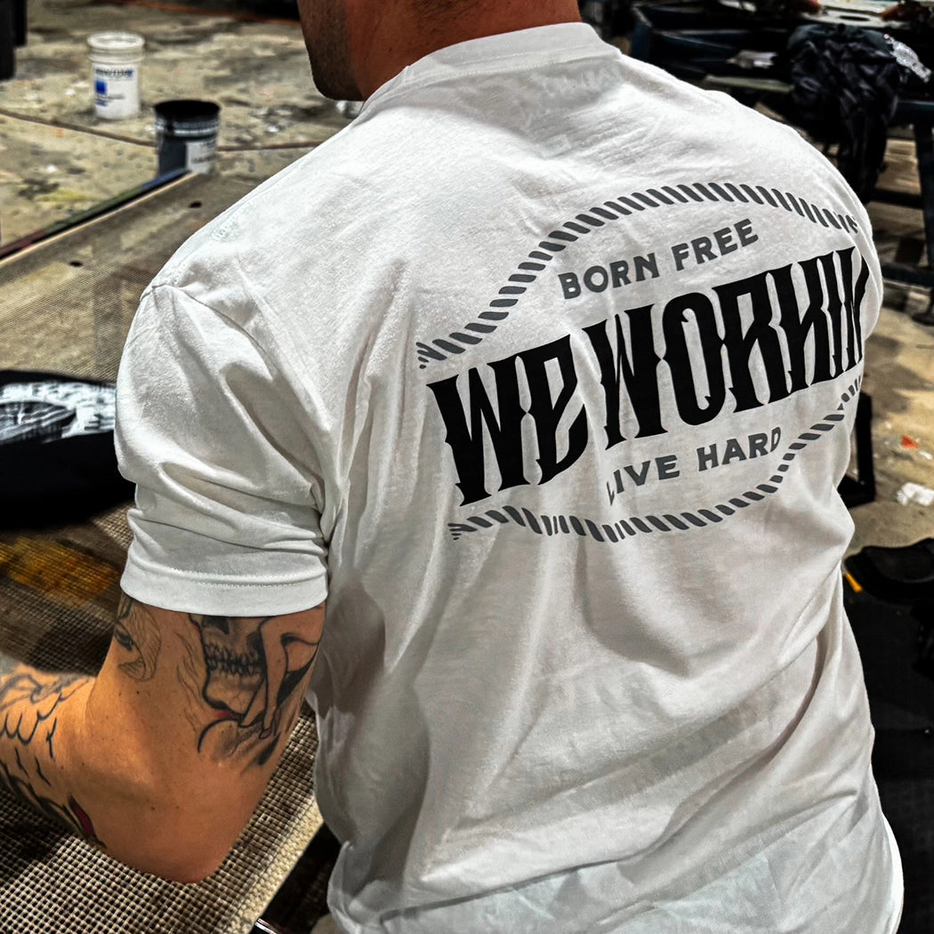 Man from back, wearing a WW white tee. "Born Free WE WORKIN Live Hard" text on 3 lines with curved rope design on the top and bottom of the text, printed large in the center/upper back, in grey and black ink.