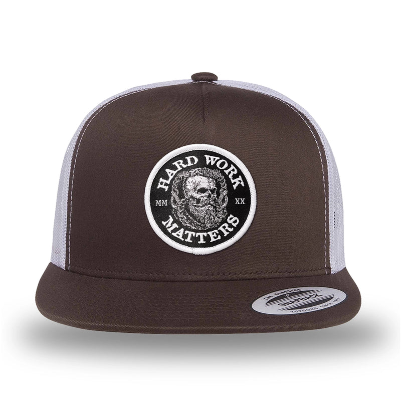 Brown/White two-tone WeWorkin hat—flatbill, snapback, 5-panel classic trucker, mesh-back style. HARD WORK MATTERS woven patch with white merrowed edge, on a black background with HARD WORK MATTERS text encircling a Viking-style skull center graphic with MM XX on the left and right respectively—patch is centered on the front panels.