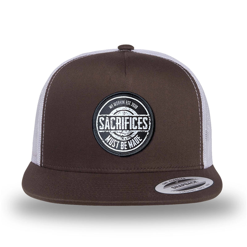Brown/White two-tone WeWorkin hat—flatbill, snapback, 5-panel classic trucker, mesh-back style. WeWorkin "SACRIFICES MUST BE MADE" circular woven patch is centered on the front panel.